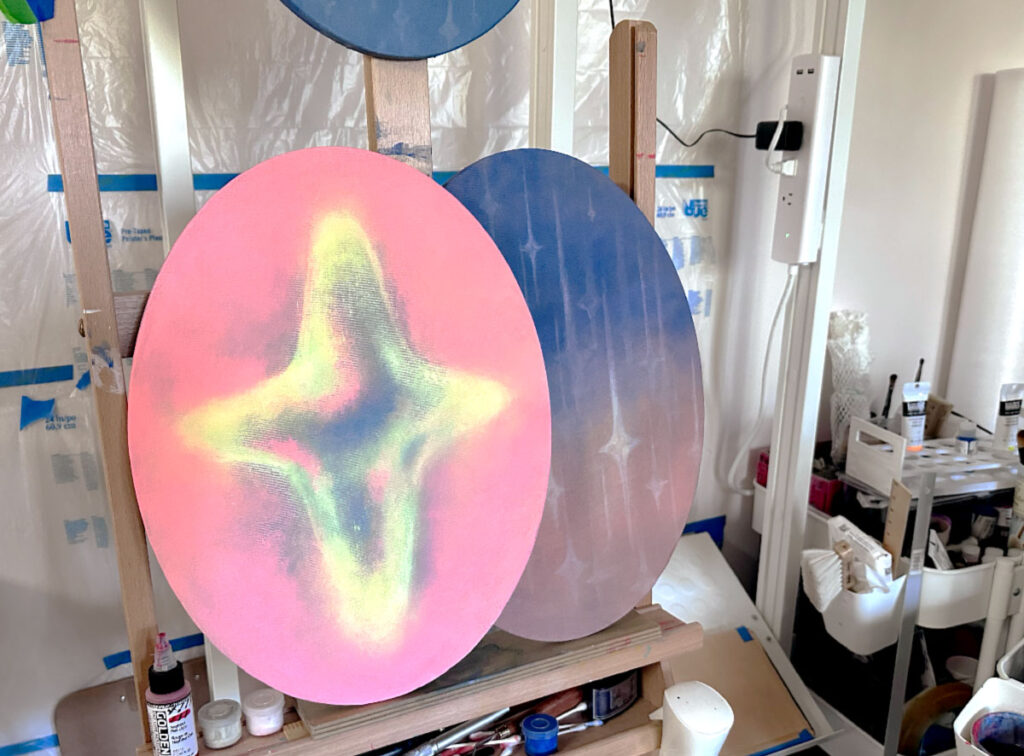 Studio view with two oval paintings on an easel. Left Tear (2024) painted in vibrant colors, right Rain (2025, work in progress) depicting tears falling like rain.