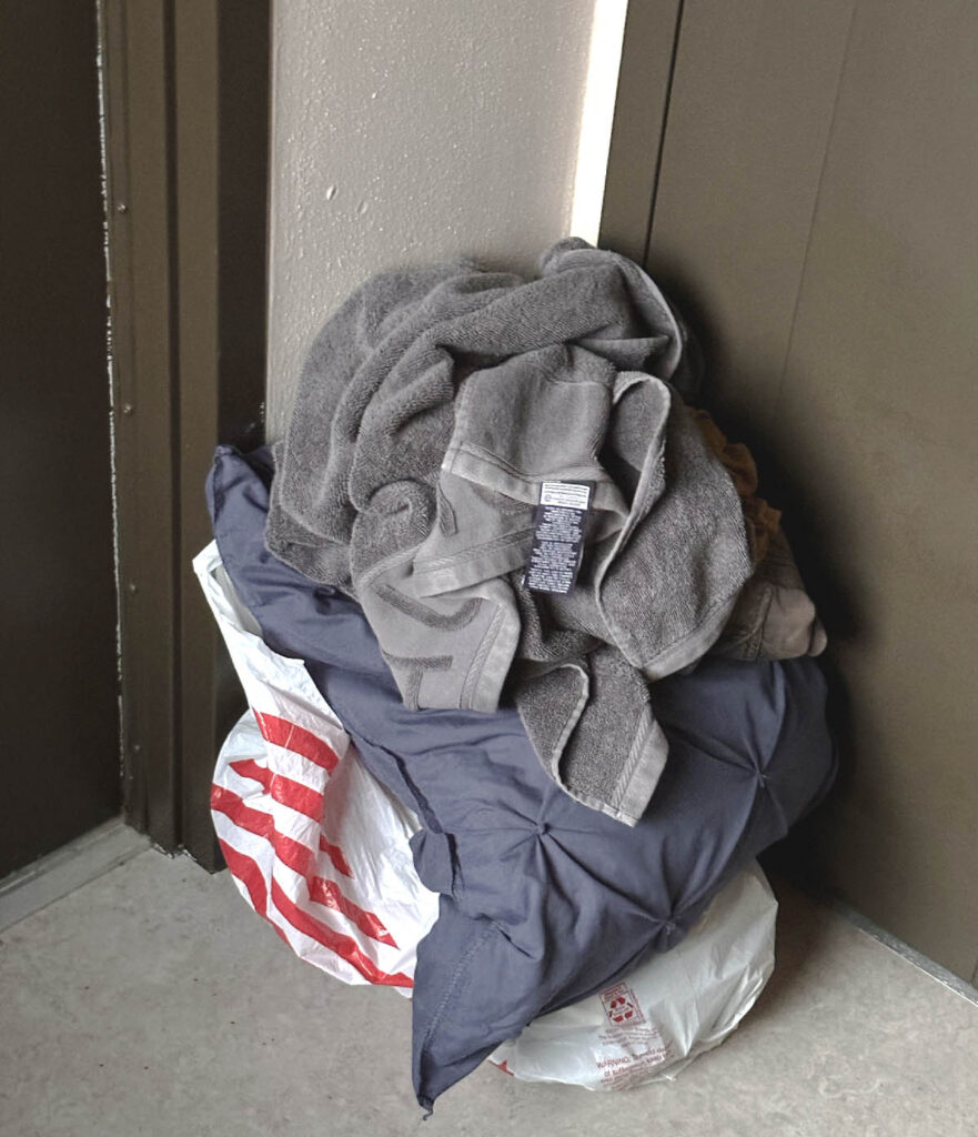 Pillow and towel placed on top of a plastic bag, left outside an apartment door.